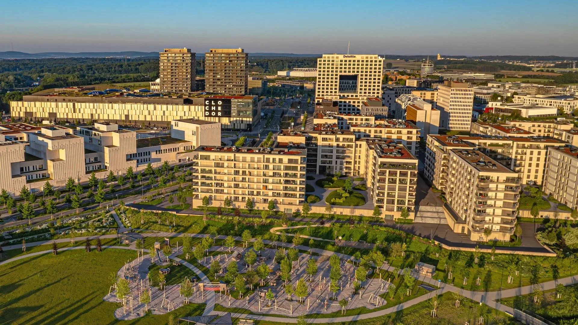 Aerial view of Gasperich Park, its paths and playgrounds, with the Cloche d’Or district behind in late-afternoon light